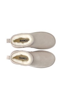 Stivaletti beige alla caviglia in suede con una morbida fodera interna in pelliccia bianca. Presentano una linguetta sul retro e un design a punta rotonda.