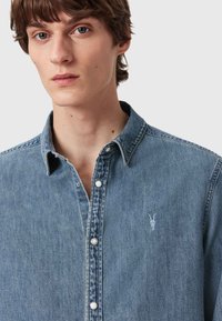 Lichtblauwe denim overhemden met een button-down kraag, witte knopen en subtiele borduursels van een geiten schedel op de linkerborst.