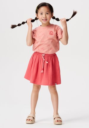 T-shirt rose à manches courtes avec imprimé « mer » ; jupe texturée corail avec taille élastique ; sandales à semelle légère.