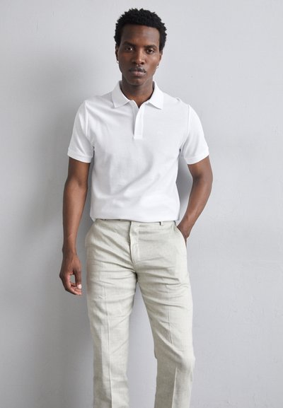 Valge lühikeste varrukatega polo särk, mis on ühendatud heleda beeži tekstuuriga pükste mugavusega. Vaatenurk keskendub lihtsale ja minimalistlikule disainile.