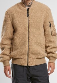 Beige fleece bomberjack met een gestructureerd oppervlak, ritssluiting, geribbelde manchetten en een zijzak met een stoffen accenten.