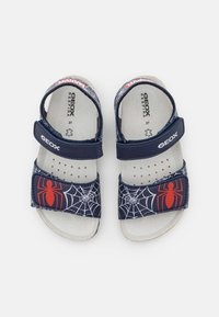 Námořnické sandály se dvěma nastavitelnými popruhy, se vzorem pavouka a pavučiny v červené a bílé barvě. Texturovaná stélka a prodyšný design.