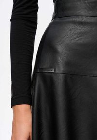 Czarna skórzana spódnica o matowej teksturze z metką oznaczoną "blue shadow". Stylizowana z czarną bluzką z długim rękawem.