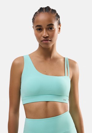 Un sujetador deportivo de color verde menta con un diseño asimétrico único, que presenta una tira ancha y una tira delgada para un detalle adicional. Textura suave.