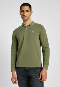 Långärmad olivgrön polo med krage, med kontrasterande vit kant och en liten Lee-logotyp på bröstet.