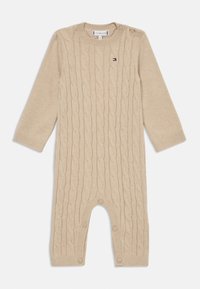 Combinaison en maille beige avec motif en câble, décolleté rond et fermetures à bouton à l'épaule et en bas. Manches longues et texture douce.