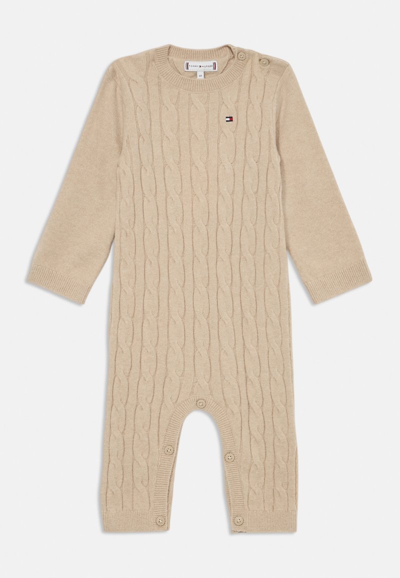 Combinaison en maille beige avec motif en câble, décolleté rond et fermetures à bouton à l'épaule et en bas. Manches longues et texture douce.