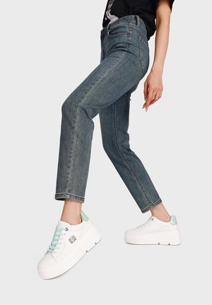 Jeans di denim blu con design aderente e gamba dritta, abbinati a sneakers bianche con plateau, caratterizzate da dettagli color menta e lacci azzurri.