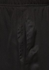 Pantalones de tela negra con cinturilla elástica y bolsillos laterales, que exhiben una textura suave y un diseño minimalista.