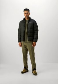 Sort vattert jakke med glidelås foran, lett design, brukt over en olivengrønn skjorte og matchende bukser, kombinert med pustende utendørs sko.