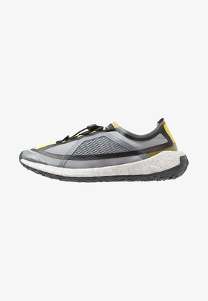 Zapatilla de running moderna gris y amarilla con panel lateral texturizado, entresuela blanca acolchada y suela exterior negra estriada, mostrada de perfil.