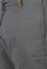 Shorts en lin gris présentant une texture lisse, un devant plat et une étiquette en cuir en accent sur la ceinture. Poches de chaque côté.