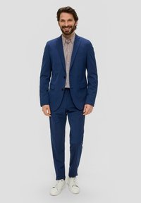 Blauwe suit met gestructureerd colbert en bijpassende broek, gedragen over een gestreept shirt. Gecombineerd met witte sneakers voor een casual uitstraling.