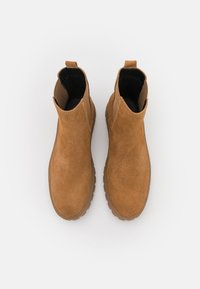 Brązowe zamszowe botki do kostki o gładkiej fakturze, niskim obcasie, elastycznych bocznych panelach i pętlach ułatwiających zakładanie. Gumowa podeszwa zapewniająca przyczepność.