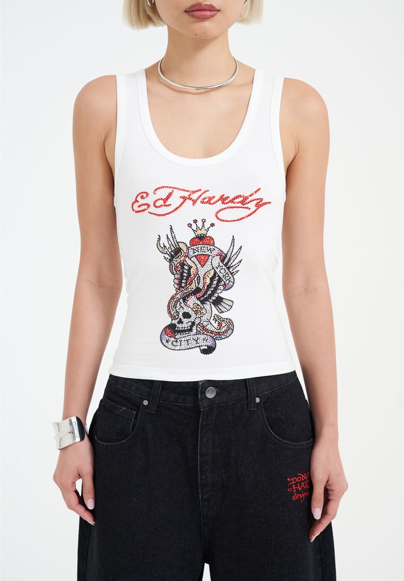 Witte tanktop met een veelkleurige strassafbeelding van een slang en schedel, met rode "Ed Hardy" tekst. Gecombineerd met zwarte broek.