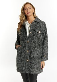 Cappotto bianco e nero a trama con colletto, chiusura a bottoni, due tasche frontali e vestibilità ampia. Presenta dettagli con bottoni in legno.