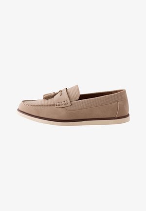Mocassin beige homme sans lacets avec pompons, dessus texturé, détails cousus et semelle blanche avec bordure marron.