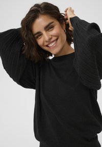 Sort striktrøje med ribbede, puffede ærmer. Stoffet har en subtil glans. Crew neck designet giver en afslappet pasform.