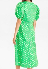 Zielona sukienka midi w białe groszki, z bufkami i dopasowaną talią. Gładka tekstura materiału, długość do kolan i okrągły dekolt.