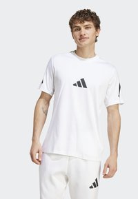 Hvit treningst-skjorte laget av stoff med rund hals, korte ermer, og to svarte Adidas-logoer på foran og på ermet.