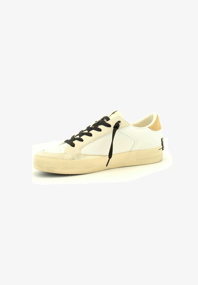 Baskets blanches avec des lacets noirs, accents en suède sur le talon, texture lisse, bout rond et semelle en caoutchouc légèrement texturée.