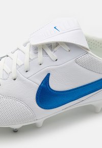 Valge jalgpallijalatse, millel on sinine Nike swoosh, perforatsioonid, traditsiooniline side ja tekstureeritud nahkpealis.