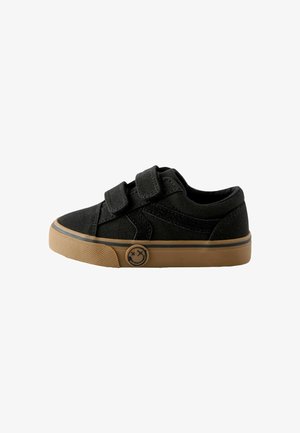Sneakers neri in tela con due cinturini in Velcro, suola in gomma color nocciola e un logo circolare con un sorriso sul lato.