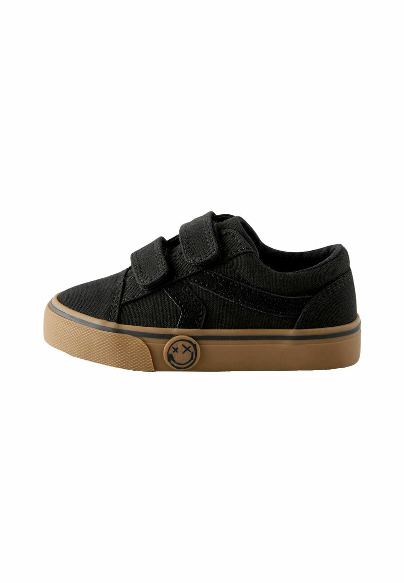 Zwarte canvas sneakers met twee klittenbandsluitingen, een tan rubberen zool en een ronde logo met een glimlachend gezicht aan de zijkant.