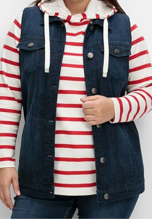 Persona che indossa una felpa con cappuccio bianca con strisce orizzontali rosse sotto un gilet di jeans blu scuro con bottoni e jeans abbinati.