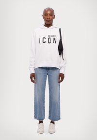 White hooded sweatshirt with "ICON" printed in black. Paired with light blue wide-leg jeans and white sneakers. Black crossbody bag.