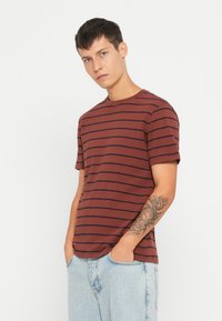 Bordeaux gestreepte t-shirt van katoen met korte mouwen, een ronde hals en blauwe horizontale strepen. Model draagt een lichtblauwe spijkerbroek.
