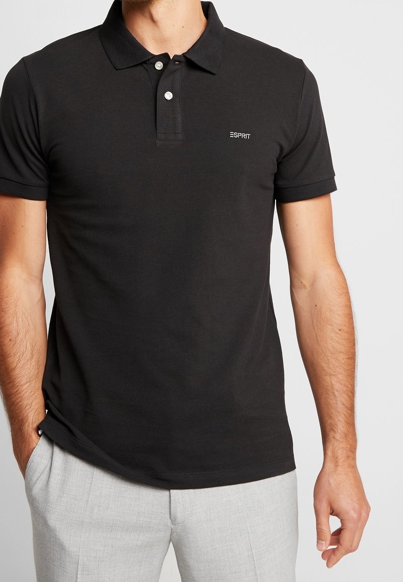 Polo noir en coton avec une finition texturée, doté d'un col, de deux boutons et d'un petit logo sur le côté gauche de la poitrine.