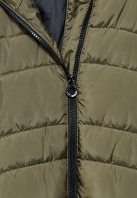 Oliwkowa puchówka z czarnym zamkiem błyskawicznym. Charakteryzuje się poziomym pikowaniem oraz gładką, błyszczącą fakturą, zaprojektowana z myślą o ciepłocie i komforcie.