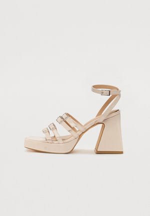Beige platform sandals with three adjustable straps and ankle buckle. Glossy finish, square heel, and smooth texture.