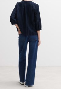 Blusa a maniche lunghe a righe navy con scollatura rotonda, con schiena arricciata, abbinata a jeans scuri a vita alta e sneakers bianche.