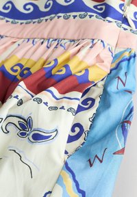 Tissu coloré avec des motifs abstraits, comprenant des volutes, des formes florales et des lettres de boussole sur un matériau froncé aux tons bleus, roses, jaunes et rouges.