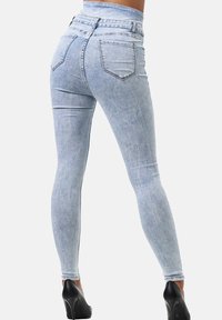 Jeans ajustados de color azul claro con una cintura alta, que cuentan con bolsillos traseros y una textura suave. Combinados con tacones altos negros para un contraste.