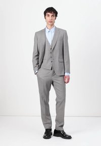 Completo grigio chiaro a tre pezzi con una finitura testurizzata, pantaloni abbinati e gilet. Abbinato a una camicia azzurra chiara e scarpe nere.