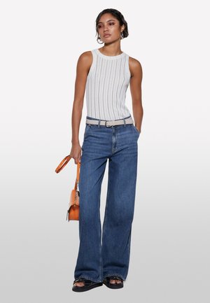 Top in cotone bianco a costine con righe verticali, jeans blu a vita alta e gamba larga, cintura intrecciata beige, sandali neri con zeppa e borsa arancione.