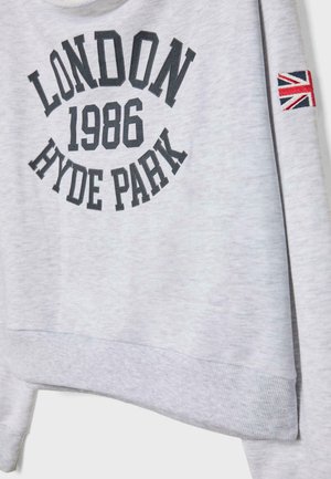 Svijetlosivi dukserica s kapuljačom na kojoj se nalazi natpis "LONDON 1986 HYDE PARK" u crnom slovu, s malom oznakom britanske zastave na rukavu i rebrastim manžetama.