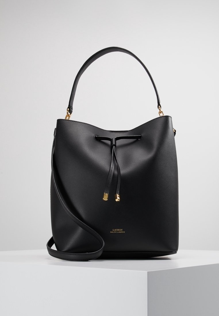 Sac seau noir en cuir lisse, avec une fermeture à cordon, un accent en métal doré et une bandoulière amovible.