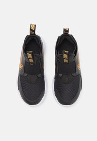 Chaussures de sport noires avec tige en mesh et synthétique, semelle en caoutchouc blanche, sangle élastique, et logo Nike en or sur le côté et sur la languette.