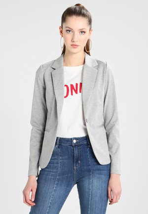 Šedý, přiléhavý blazer s klopami přes bílé tričko s červeným textem, spárovaný s modrými džíny s vysokým pasem.