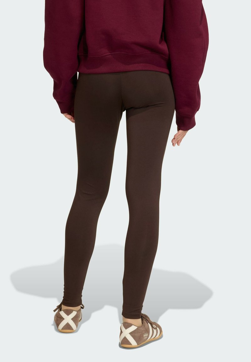 Leggings marroni con una texture liscia, caratterizzati da una vita alta e una silhouette aderente, abbinati a una felpa oversized color bordeaux e scarpe marroni.
