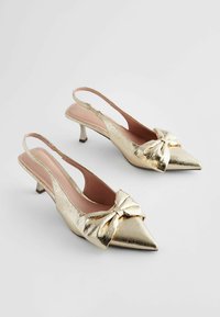 Kultaiset metalliset slingback-kengät, joissa on teräväkärkinen muoto ja nauhakoriste etuosassa. Ominaisuuksiin kuuluu pieni peruskorot ja sileä pinta.