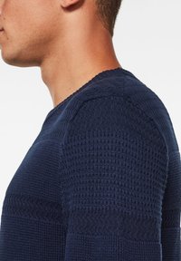 Marineblauer Strickpullover mit strukturierten Mustern an Schulter und Körper, ausgestattet mit einem Rundhalsausschnitt und gerippten Ärmelsäumen.