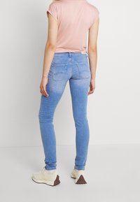 Ljusblå tajta jeans med en blekt textur, utrustade med bakfickor och midjehöjd i midjan, kombinerade med vita sneakers och en rosa topp.