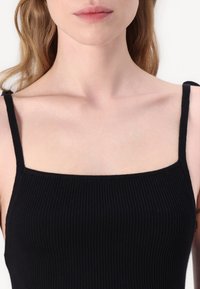 Svart ribbet tank topp med tynne skulderstropper og firkantet hals, laget av et mykt, elastisk stoff.