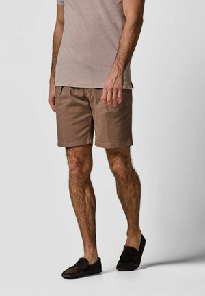 Braune Baumwollshorts mit lockerer Passform, Seitentaschen und weicher Textur. Kombiniert mit einem hellen T-Shirt und dunklen Slip-on-Schuhen.