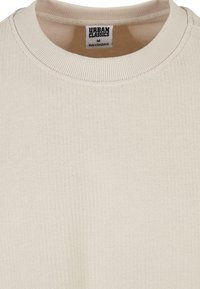 Beige geribbelde langemouwshirt met een ronde hals en een label waarop "URBAN CLASSICS" en "Made in Bangladesh" staat.